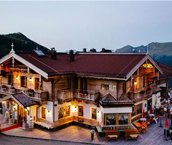 Ein charmantes Berghotel mit Holzfassade und Balkon. Die Umgebung ist malerisch mit Bergen im Hintergrund.