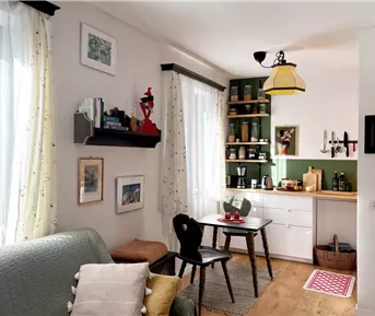Ein gemütliches Wohnzimmer mit einer kleinen Essecke und einer Küche im Hintergrund. Helle Farben und eine einladende Atmosphäre prägen den Raum.