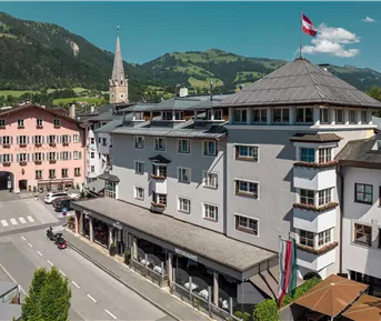 Eine malerische Stadt mit traditionellen Gebäuden und einer Kirche im Hintergrund. Die Berge und der klare Himmel schaffen eine einladende Atmosphäre.