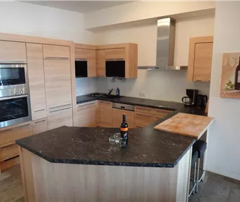 Eine moderne Küche mit holzfarbenen Schränken und dunkler Arbeitsplatte. Im Hintergrund sind Kochgeräte und ein Weingemälde zu sehen.