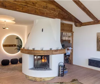 Ein modern eingerichteter Wohnraum mit einem runden Kamin im Mittelpunkt. Holzdecken und eine gemütliche Atmosphäre schaffen einladende Eleganz.