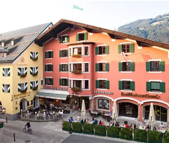 Ein schönes, buntes Gebäude mit einem Restaurant und vielen Terrassenplätzen. Menschen genießen das Essen draußen in einer malerischen Umgebung.