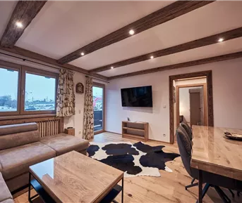 Ein modernes Wohn- und Esszimmer mit Holzböden und gemütlicher Möbelgestaltung. Große Fenster sorgen für viel Tageslicht.